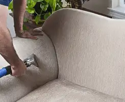 Professional upholstery cleaner deep-cleaning a fabric sofa with a handheld extraction tool and hose in Arlington, TX.